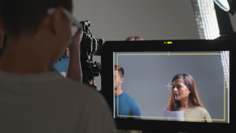 Female-Film-Director-Watching-Male-And-Female-Actors-With-Scripts-Rehearsing-For-Shooting-Movie-Or-Video-In-Studio-On-Monitor